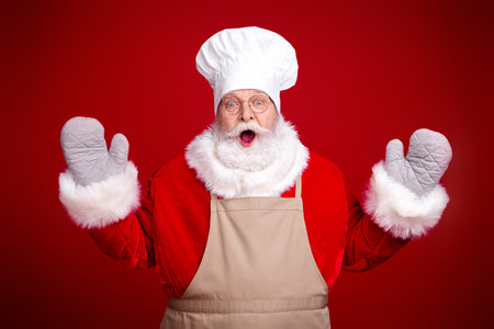 Santa chef in red suit with white beard apron and chef hat poses for festive holiday scenes in a warm studio setting ready to cook celebrateの写真素材