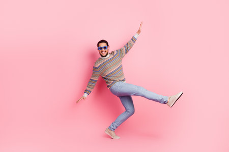 Stylish young man in colorful sweater and sunglasses posing energetically against pastel pink backgroundの写真素材