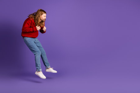 Young man jumps in casual fashion against purple background making a dynamic lifestyle statementの写真素材