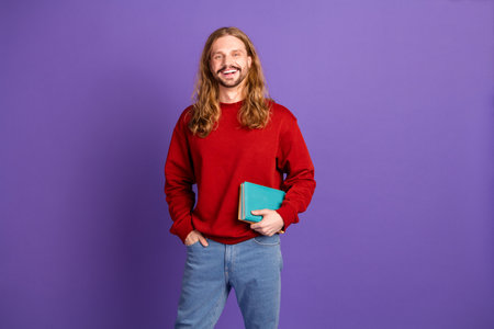 Young handsome male student with long blonde hair in casual red sweater smiling against purple...