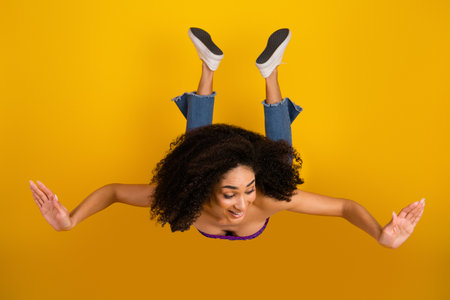 Young woman jumps with arms outstretched against a bold yellow background showcasing casual chic...