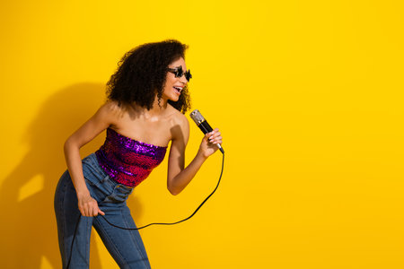 Young woman singer performs with microphone against bright yellow background exuding glamour chic...
