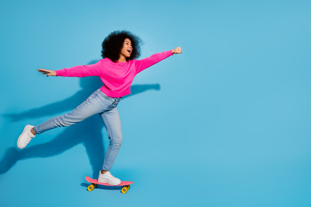 Young woman in stylish casual outfit skateboarding joyfully against a bright blue background, enjoying leisure time.の写真素材