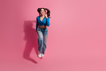 Young woman jumping on a pink background in a vibrant outfit exuding joy and energy, with an engaging hairstyleの写真素材