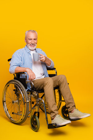 Grandpa in a wheelchair enjoying a warm mug in a bright yellow studio setting with a friendly and relaxed posture conveying comfort accessibility and inclusion in a positive health care themed sceneの写真素材