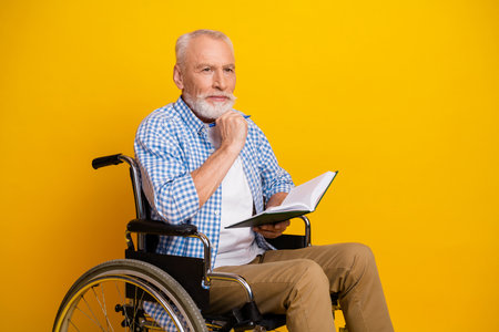 Grandpa in wheelchair studies notes and smiles in bright yellow studio creating warm inclusive rehab...