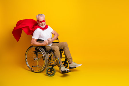 Funny senior superhero in wheelchair cape and mask smiles on bold yellow backdrop bringing hope and humorの写真素材