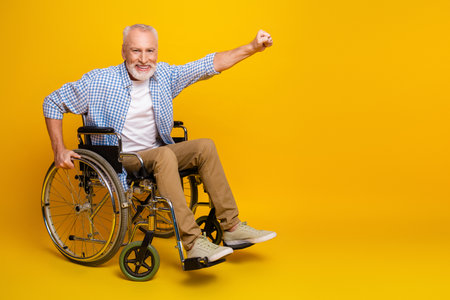 Grandpa in a wheelchair celebrates strength and joy in a bright yellow studio proving disability can be vibrant and hopefulの写真素材