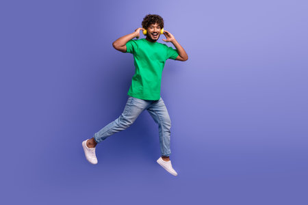 Young man in casual green t-shirt and jeans posing cheerfully against a vibrant purple backgroundの写真素材