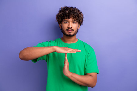 Positive casual male making a timeout gesture against a simple vibrant purple background showcasing green fashion.の写真素材
