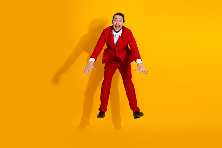Funny businessman leaps in a red suit against a bright yellow background for a bold energetic stock image with stylish vibesの写真素材