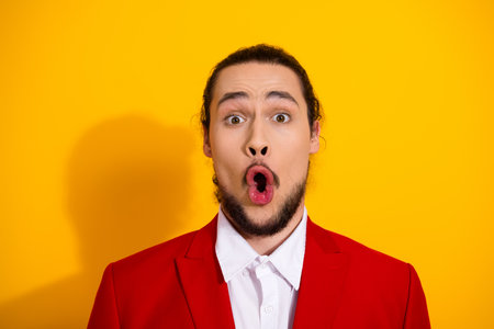 Surprised man in red suit on a bright yellow backdrop creates a funny stylish moment perfect for fashion ads and holiday promotionの写真素材