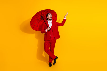 Hilarious stylish entertainer in bold red suit with umbrella striking a playful pose against bright yellow background for striking fashion and advertising impactの写真素材