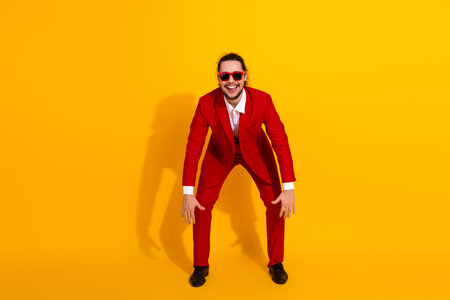 Playful man in red suit poses for bold fashion portrait on bright yellow backdrop with stylish flair and comedic energyの写真素材