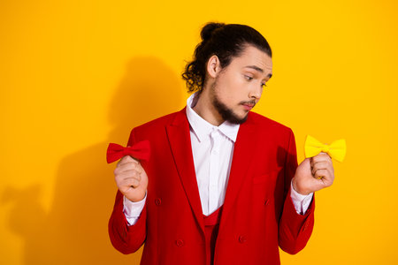 Funny stylish man in red suit holds red bow and yellow bow in a bold fashion moment for a festive promoの写真素材