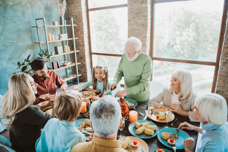 Heartwarming family feast around a sunny table with grandparents grandchildren sharing laughter and gratitude during a cozy Thanksgiving gatheringの写真素材