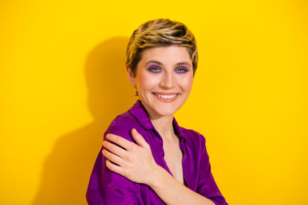 Young stylish woman with short blonde hair in a purple blouse smiles against a bright yellow...