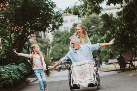 Funny park day with grandpa in wheelchair smiling while family cheers and daughter runs besideの写真素材