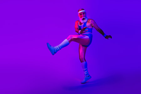 Energetic retro sportsman with beard in blue jumpsuit kicks mid air under neon purple studio lights and vibrant fashion vibeの写真素材