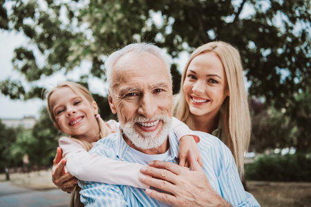 Family moment outdoors with grandpa daughter and girl smiling in park cheerful embrace and warm bond among loved onesの写真素材