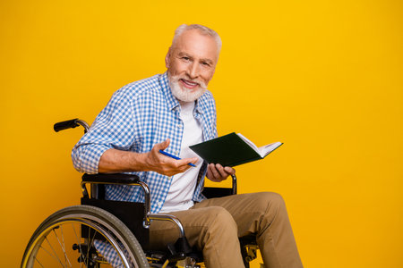 Cheerful grandpa in a wheelchair reads a book and smiles bright during rehab day in sunny studio