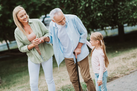 A heartwarming family moment outdoors as grandpa and granddaughter support an elderly man on a walk in the parkの写真素材