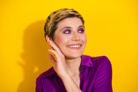 Young glamorous woman with short blonde hair in a purple blouse smiles against a bright yellow backgroundの写真素材