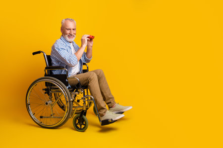 Playful grandpa in a wheelchair enjoying a bright yellow studio moment full of warmth humor and resilienceの写真素材