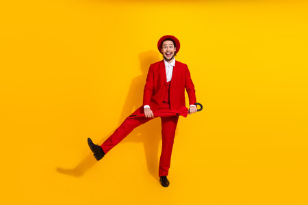 Funny stylish man in a red suit kicks leg against bright yellow background showing charm energy and fashionの写真素材