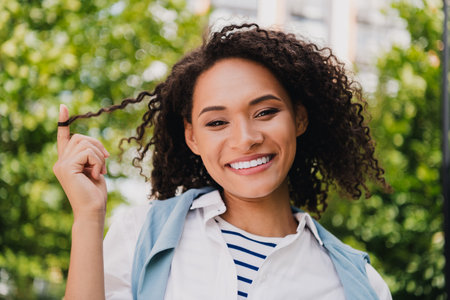 Happy young woman smiling outdoors in sunny park wearing striped shirt and light jacket enjoying a...