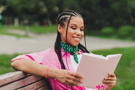 Young girl with braids reading a notebook on a park bench enjoying outdoor leisure and fashion in a sunny park settingの写真素材