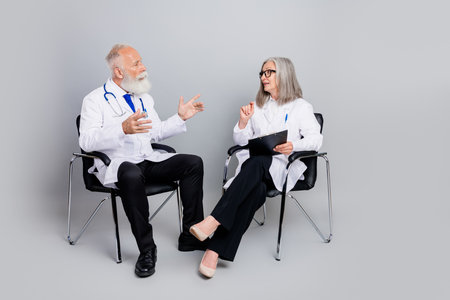 Two experienced doctors in white coats discuss patient care treatment options during professional consultation in a modern clinic settingの写真素材