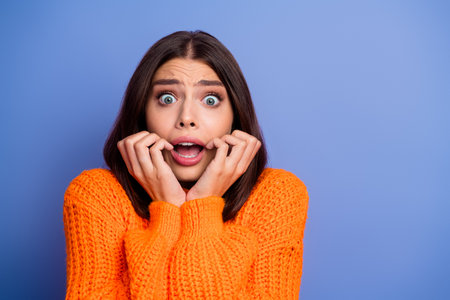 Young woman in orange sweater showing surprised expression for seasonal autumn fashion against vibrant blue backgroundの写真素材