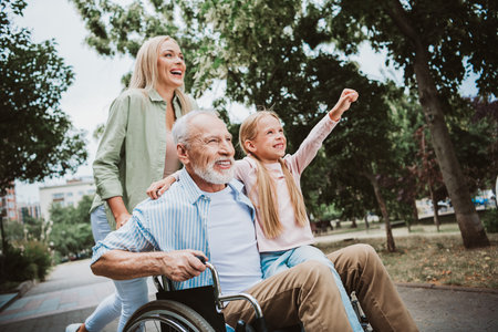 Family park joy as grandpa in wheelchair is cared for by daughter and granddaughter in a warm reunionの写真素材