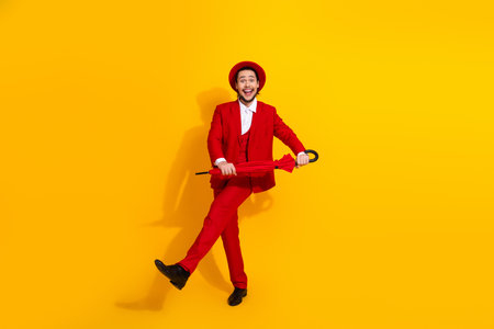 Funny stylish man in red suit dances with umbrella against bright yellow background for a bold fashion advertisementの写真素材