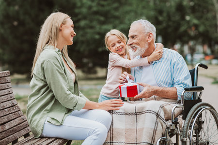 A heartwarming family moment in the park as a granddaughter gives a gift to grandpa in a wheelchair...