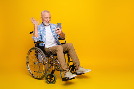 Funny grandpa on wheelchair texting joy at colorful yellow studio a lighthearted moment of accessibility inclusion and everyday health care compassion and connection with familyの写真素材