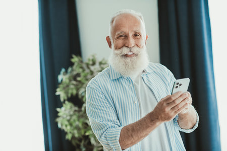 Smiling senior man with a phone in a cozy home interior enjoying a casual moment at home