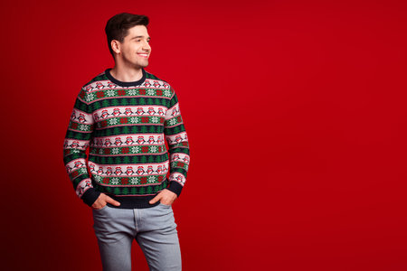 Man in festive Christmas sweater smiles on a red background ready for holiday cheer and seasonal shoppingの写真素材