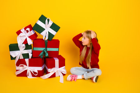 Funny delightful scene of a kid among big gift boxes smiles and laughs as Christmas magic fills a bright yellow roomの写真素材