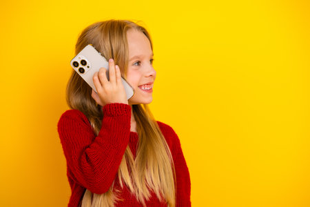 Playful kid on a sunny day talking on phone with big smile wearing red sweater against a bright yellow backdropの写真素材