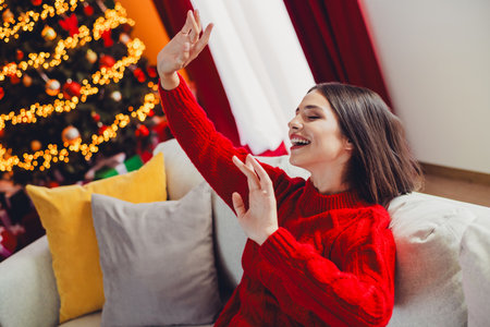 Dancing with joy at home a woman in red sweater celebrates Christmas beside a lit treeの写真素材