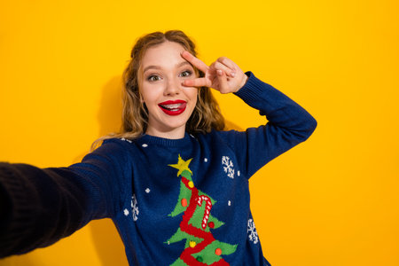 Cheerful young woman in festive sweater posing against vibrant yellow background, sharing holiday joy and Christmas spiritの写真素材