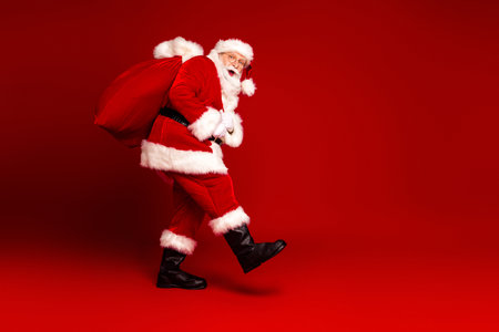 Santa carries a large red bag and dances in a bright red studio for a festive Christmas scene perfect for holiday campaigns and family promotionsの写真素材
