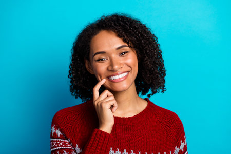 Smiling young woman in red sweater with curly hair against blue background ready for holiday shopping and Christmas cheerの写真素材