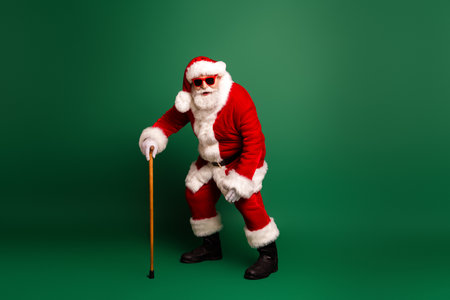 Santa with cane in classic red suit and white fur trim smiles in front of green background for festive holiday promotionの写真素材