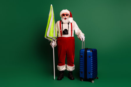 Santa in red suit with camera and props ready for holiday travel and Christmas style photo shoot on green backgroundの写真素材