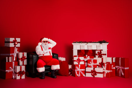 Santa Claus relaxes in a red room surrounded by presents and a festive mantel during Christmas Eve celebrationの写真素材