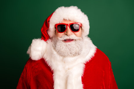 Smiling Santa in red suit with white beard and trendy hat delivers festive cheer for christmas against green background holiday campaigns promotionsの写真素材