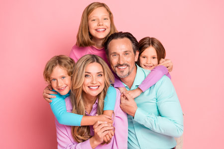 Joyful family portrait of parents and children smiling together against a pink background celebrating love and togethernessの写真素材